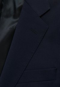 Marinblå skräddarsydd kavaj med slät yta, med en urklippt krage och en ficka. Fodret är av svart satin.