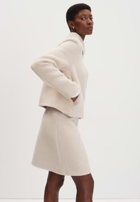 Beige wollen mix trui met een hoge kraag en verlaagde schouders, gecombineerd met een aansluitende beige rok tot de knie. Soepele textuur, minimalistisch ontwerp.