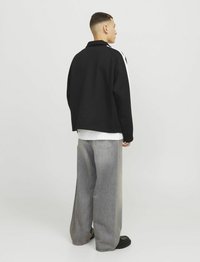 Sort og hvid fleecejakke med krave, parret med løse, lysegrå jeans og sorte sko. Enkel design uden synlige mønstre.