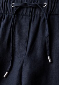 Detailní záběr na námořnicky modré látkové kalhoty se stahovací šňůrkou protaženou kovovými očky a kovovými koncovkami na koncích.