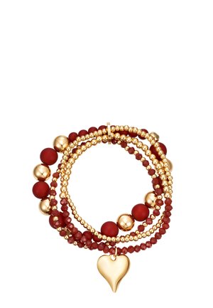 Gestapelte Perlenarmbänder in Gold und Dunkelrot, mit glatten und facettierten runden Perlen und einem goldenen Herzanhänger, der an einem Armband hängt.