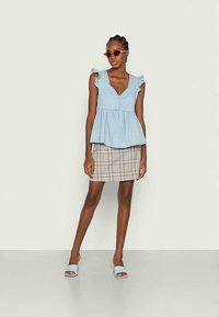 Top peplum azul claro com mangas rendadas, combinado com uma saia mini xadrez. Usado com sandálias de slide azul claro e óculos de sol cor-de-rosa.