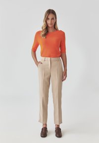 Orange knit sweater with short sleeves, beige tailored trousers, and brown loafers. Smooth texture and fitted design.