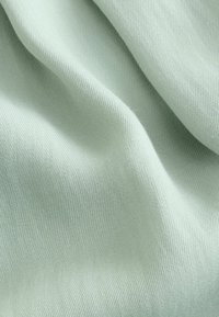 Soft light green fabric with visible fine diagonal weave, shown in gentle folds creating subtle shadows and texture.