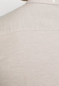 Lichtbeige linnen overhemd met een subtiele textuur, voorzien van een button-down kraag en een schoon, eenvoudig ontwerp. De achterkant toont naadafwerking.