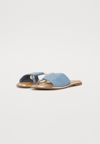 Blå sandle med flat såle, laget av glatt materiale. Har en bred overdel og dekorative hardware- accenter. Gull detaljer på sålen.