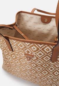 Borsa intrecciata beige con un motivo a rombi, dettagli in pelle marrone e una placca con il logo. L'interno presenta un tessuto beige con il nome del marchio ripetuto.