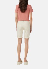 Jasnoróżowa koszulka z krótkim rękawem w połączeniu z kremowymi dżinsowymi szortami z podwiniętymi rękawami oraz jasnymi sandałami na platformie; widoczne tylne kieszenie w szortach.