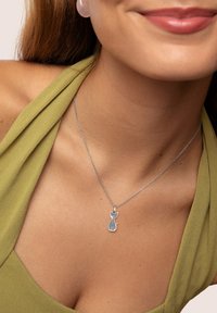 Silver katt berlock på ett fint kedja, bärs med en grön halterneck-topp, vilket framhäver halsbandets intrikata design och rena linjer.