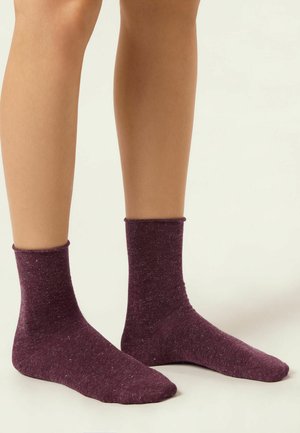 Knöchelsocken in einem tiefen lila Farbton, gefertigt aus einem strukturierten Stoff mit kleinen Flecken. Bequeme Passform mit einem dehnbaren, gerippten Bündchen.