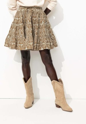 Jupe brune à motifs avec un design paisley blanc, volants en couches et une taille élastique. Assortie à des bottes de cow-boy en suède beige.