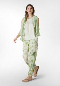 Helles grünes, ärmelloses Oberteil mit Blumendruckhose in verschiedenen Grüntönen und Creme. Flip-Flops. Weicher, fließender Stoff mit lockerer Passform.