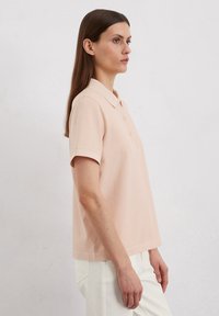 Lichtroze polo shirt met korte mouwen, een kraag en drie knopen. Zacht katoen, rechte snit, minimalistisch ontwerp.