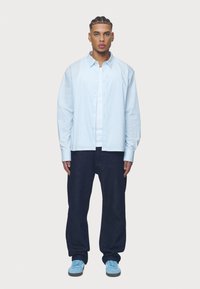 Svetlomodrá pruhovaná košeľa na gombíky, voľné tmavé džínsy a modré tenisky. Medzi vlastnosti patrí golier, manžety s nápletmi a uvoľnený strih.