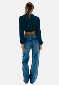 Blusa cropped blu scuro con maniche a sbuffo e dettaglio a chiave sul retro, abbinata a jeans in denim chiaro a vita alta e gamba larga.