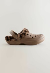 Ruskeat tikkukengät, joissa on tekoturkisreunus, ilmanvaihtoaukot ja takanauha. Tasainen muovimateriaali, jossa on teksturoitu pinta.