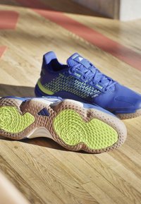 Blauwe sportieve schoenen met een gestructureerde mesh bovenkant, met groene accenten en een geprofileerde rubberen zool in lichtbruin en limoengroen.