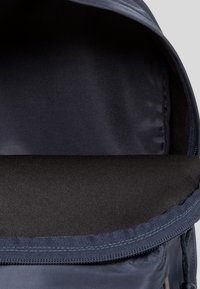 Sac à dos bleu foncé ouvert montrant un compartiment principal vide doublé de tissu noir et une fermeture éclair partiellement visible.