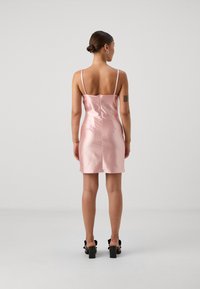 Pink satin mini dress with thin straps, form-fitting design, smooth texture, zip closure at the back, paired with black block-heeled sandals.