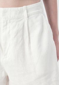 Pantaloni bianchi in lino con vita, pieghe piegate e tasche laterali, caratterizzati da una superficie morbida e testurizzata.