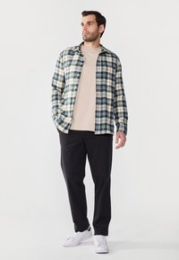 Rutet flanellskjorte i grønn, marineblå og krem, båret over en beige t-skjorte; kombinert med svarte bukser og hvite sneakers.