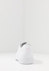 Zapatilla blanca con parte superior de cuero texturizado, detalles grises y logotipo rosa en la parte trasera. Cuenta con interior acolchado y suela plana.