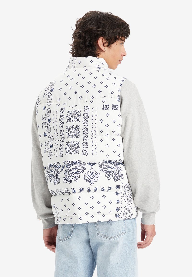Chaleco hinchado blanco con estampado de pañuelo en color navy, con patrones de paisley y geométricos, cierre de cremallera y mangas largas grises debajo.