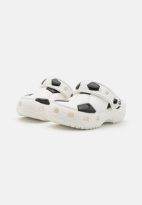 Tamancos brancos com padrões de bolas de futebol pretas, feitos de plástico moldado, com orifícios de ventilação e correias ajustáveis para um ajuste seguro.