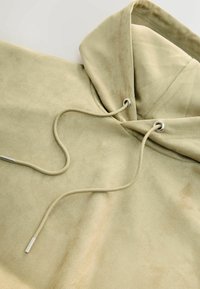 Beżowa bluza z kapturem wykonana z miękkiego, teksturowanego materiału. Posiada sznurek ze metalowymi końcówkami oraz luźny krój.
