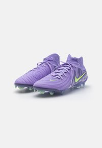 Botas de fútbol moradas con material texturizado, diseño de media caña, acentos verdes y tachuelas de plástico sobre una suela translúcida.