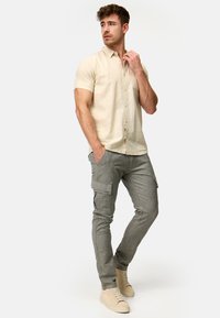 Camisa de botones de manga corta en color beige claro combinada con pantalones de carga grises ajustados que cuentan con bolsillos laterales. Modelo lleva zapatillas beige.
