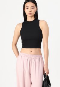 Top nero senza maniche e corto con colletto alto, abbinato a pantaloni larghi di un rosa chiaro, tenuti con una borsa nera.