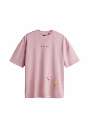 Lyserød t-shirt med korte ærmer med gul "DE LA SOUL" tekst og to små blomst illustrationer nær nederste højre side.