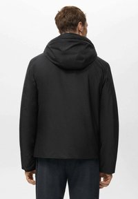 Giacca nera con cappuccio e texture liscia, caratterizzata da una vestibilità comoda e un design minimalista. La parte posteriore presenta cuciture sulle spalle e nessuna ferramenta visibile.