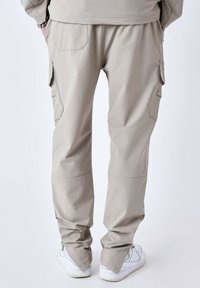 Pantalones cargo beige con un fit relajado, que cuentan con bolsillos laterales, puños elásticos y una textura suave. Los pantalones se ajustan hacia los tobillos.