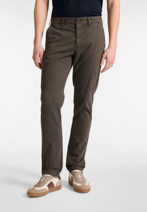 Brown, slim-fit trousers made of smooth fabric, featuring a classic five-pocket design and a single button closure, paired with beige sneakers.