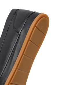 Zapato de cuero negro con costuras visibles y una suela gruesa de goma marrón con ranuras para tracción.