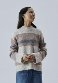 Dryžuotas megztinis su apvalia iškirpte, pagamintas iš minkštos, pūkuotos medžiagos. Spalvos apima kreminę, rožinę ir mėlyną. Yra plačios rankogaliai ir laisvas siluetas.