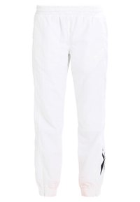 Bílé sportovní kalhoty s elastickým pasem a manžetami u kotníků, se černou hvězdou na přední části dolní pravé nohy.