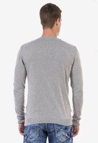 Grauer Langarmpullover mit rundem Ausschnitt, gerippten Bündchen und Saum, von hinten gezeigt. Über blauen Jeans mit Rückentaschendesigns getragen.