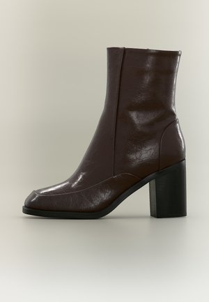Bottine en cuir marron foncé avec bout carré et talon bloc noir épais sur fond clair.