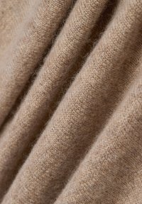 Tissu en cachemire beige, en tricot doux et fin, présentant une texture lisse avec des fibres visibles et des plis délicats.