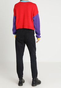 Sweter dziany z czerwonymi, fioletowymi i niebieskimi sekcjami; czarne dżinsy z wysokim stanem; noszone z czarnymi botkami; gładka faktura i luźny krój.