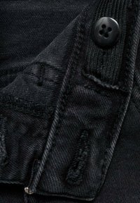 Svart denimtyg med en strukturerad yta, med knappstängning, kontrasterande sömmar och subtila slitningar i kanterna.