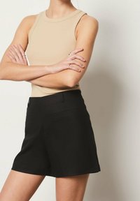 Beige ribbad ärmlös topp med rund halsringning kombinerad med svarta skräddarsydda shorts med sidofickor och slät textur.