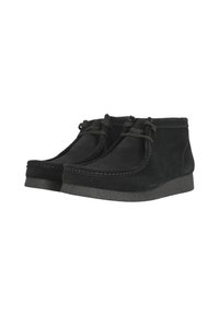 Botas de tobillo de ante negro con suela de goma, que presentan costuras mínimas y cordones en la parte delantera. Punta redondeada y textura suave.