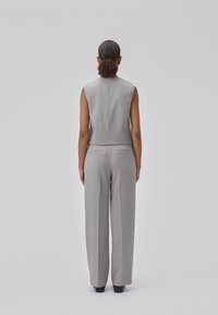 Top sans mâne de culoare gri deschis, ajustat, și pantaloni cu picioare largi, având cusături discrete pe spate și buzunare, confecționati dintr-un material neted și structurat.