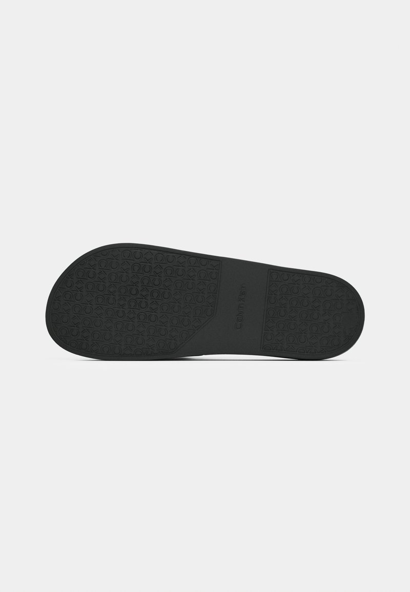 Semelle de chaussure en caoutchouc noir avec motif de grip texturé et logo en relief, forme plate, bords lisses, couleur uniformément répartie sur l'ensemble de la surface.