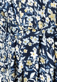 Das navyfarbene Blumenmuster des Kleides zeigt kleine gelbe und hellblaue Blumen, hat eine strukturierte Oberfläche und eine taillierte Silhouette, die durch einen Gürtel betont wird.