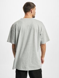 Camiseta de algodón gris con un ajuste holgado y mangas cortas. Presenta un cuello redondo y una textura lisa, mostrada desde la vista trasera.